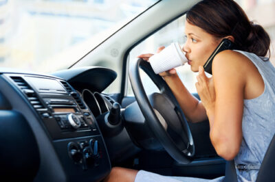 Distracted woman drinking coffee and talking on the phone while driving